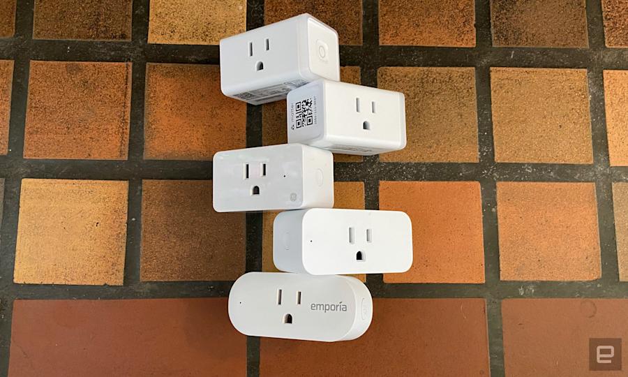 Five smart plugs from TP-Link, Amazon, Emporia and GE are stacked on a yellow, orange and brown tiled surface. 
